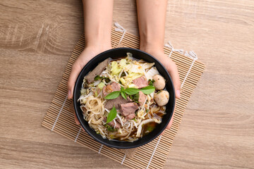 Rice noodle soup with pork, pork ball and vegetables in a bowl holding by hand, Thai noodles soup