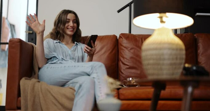 Young woman control light, switching floor lamp with a smartphone while sitting on a sofa at home. Smart home concept