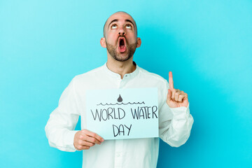 Young caucasian bald man celebrating world water day isolated on blue background pointing upside with opened mouth.