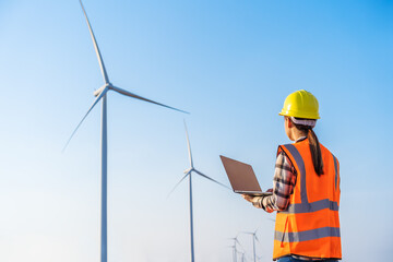female engineer working with laptop computer against wind turbine farm