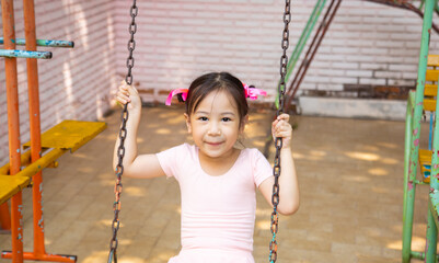 Portrait of adorable and pretty asian girl in pink ballet dress playing alone in playground for swing and climbing shows happiness and enjoyment outdoor activity of children with positive thought