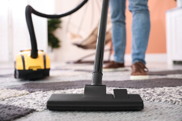 Young man cleaning carpet with vacuum cleaner at home, closeup