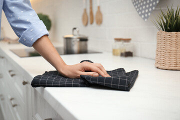 Woman wiping white table with kitchen towel, closeup