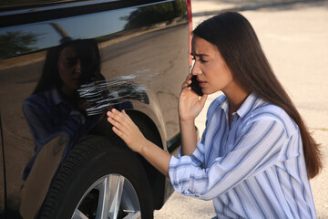 Stressed woman talking on phone near car with scratch outdoors