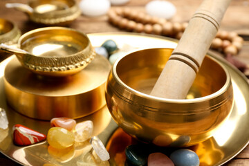 Golden singing bowl with mallet and healing stones on tray, closeup