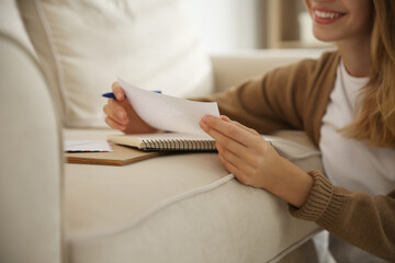 Happy woman writing letter on sofa at home, closeup