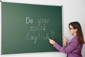 Teacher near green chalkboard with words Do You Speak English?