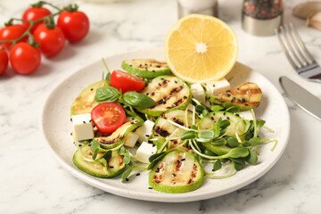 Delicious grilled zucchini slices served with feta cheese, tomatoes and lemon on white marble table, closeup