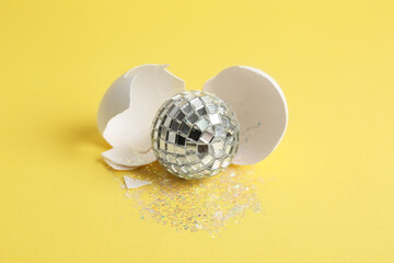 Silver disco ball, broken eggshell and glitter sprinkles on yellow background