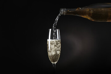 Pouring sparkling wine from bottle into glass on black background