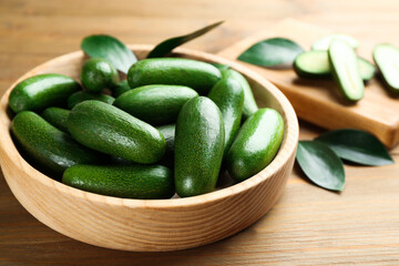 Fresh seedless avocados with green leaves in bowl on wooden table, closeup