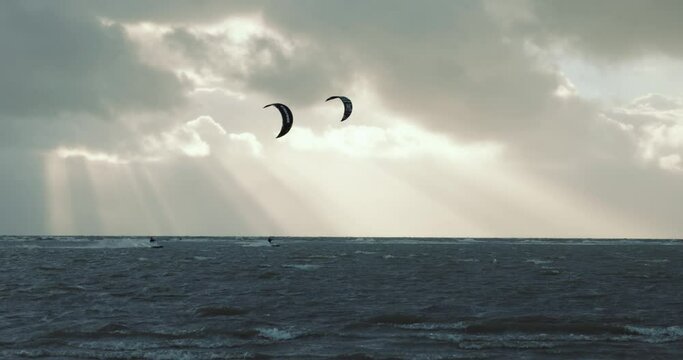 Kitesurfers shredding in storm, while sun beams through dark clouds