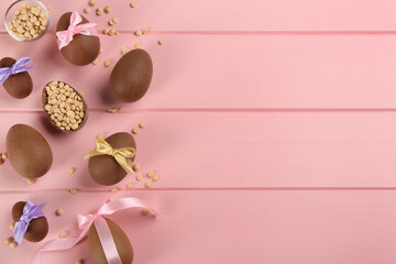 Sweet chocolate eggs and candies on pink wooden table, flat lay. Space for text
