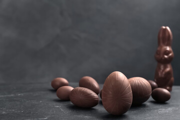 Sweet chocolate eggs and bunny on black table. Space for text
