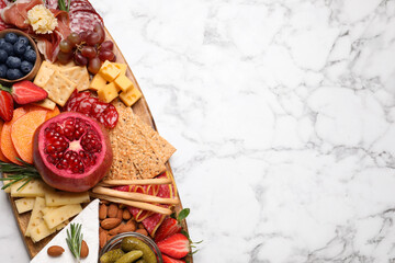 Wooden plate with different delicious snacks on white marble table, top view. Space for text