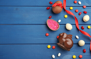 Chocolate Easter bunny, candies and eggs on blue wooden table, flat lay. Space for text