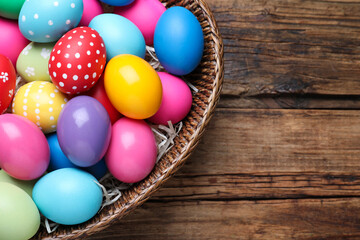 Fototapeta na wymiar Colorful Easter eggs in wicker basket on wooden table, top view. Space for text