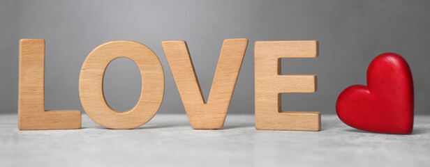 Word Love made of wooden letters near red decorative heart on light table