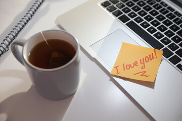 Sticky note with handwritten text I Love You attached to laptop at workplace. Romantic message