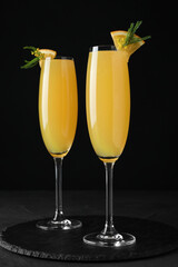 Glasses of Mimosa cocktail with garnish on black table