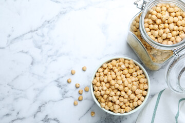 Bowl and jar with chickpeas on white marble table, flat lay. Space for text