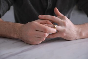 Fototapeta premium Man taking off wedding ring at white marble table, closeup. Divorce concept