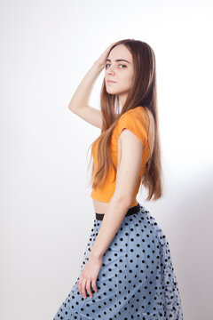 Beautiful slim young young girl teenager with long blond hair in a yellow tank top and a blue skirt with black polka dots. Photo in the studio.