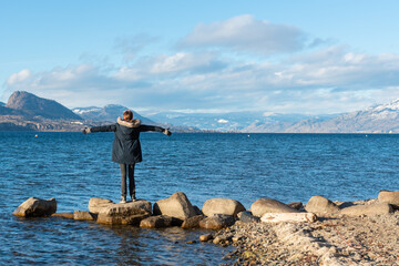Woman standing on shore of Okanagan Lake in sunny winter afternoon