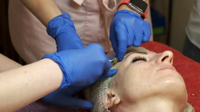 Training of young personnel. Close-up of a beautician's hand in blue rubber gloves giving injections to a woman's face with a syringe. PRP rejuvenation of the face.