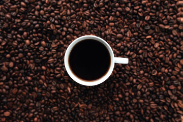White cup of coffee on a bunch of roasted coffee beans background