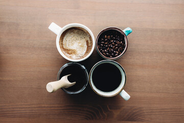 Multiple coffee cups, milk, beans and ground coffee in jar on wooden background