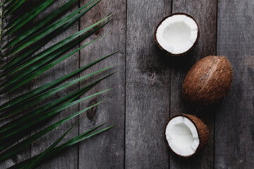 Broken coconuts on gray wooden background with palm leaf. White coconut pulp