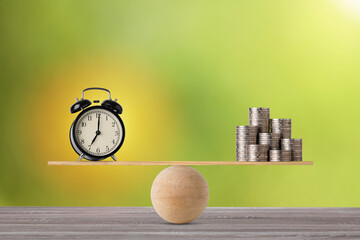 Alarm clock on seesaw balancing with stacking coins money on wooden table, meaning of business...