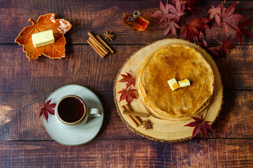 Thin Russian pancakes (crepes) with maple syrup and tea on a wooden table. Leaves, anise stars and cinnamon sticks are placed on the board as decoration. Autumn atmosphere.