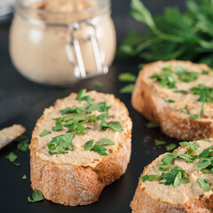 Extreme close up view of slice bread with homemade turkey pate and fresh green parsley on black kutting board over black cement background, Shallow DOF. Selective focus