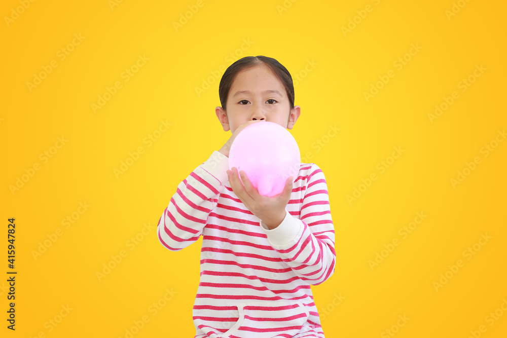 Wall mural pretty asian little child girl blowing balloon isolated on yellow background with clipping path