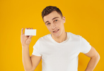 guy in white t-shirt showing business card on yellow background cropped view