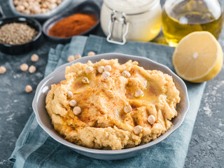 Homemade hummus with olive oil in gray bowl and ingredients. Traditional middle eastern appetizer hummus on gray background - healthy vegan paste snack. Vegetarian diet,nutrition protein food concept
