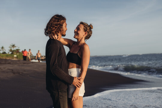 On the ocean on the black sand stands a couple lovingly looking at each other. High quality photo