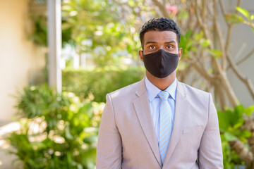 African businessman with face mask for protection outdoors looking at camera