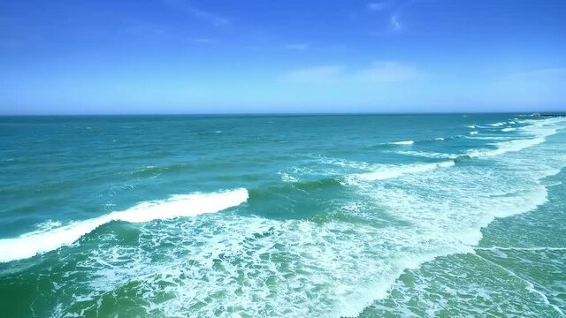 On the vast and boundless sea, waves rushing toward the coast under the blue sky