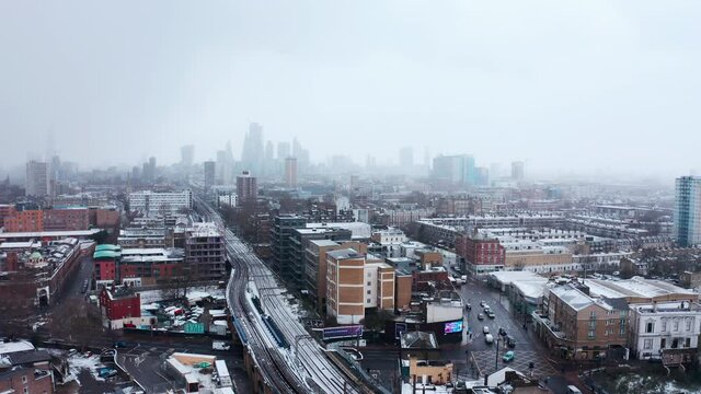 Circling aerial shot of train tracks covered in show heading towards city of London skyscrapers