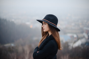 Side view of woman in hat standing at dark autumn park