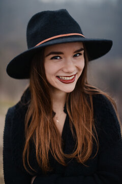 Portrait of smiling brunette in black hat posing at park