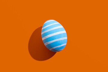 Easter art. Festive ornament. Spring holiday card. Handmade decoration. Abstract background. Blue egg with white pattern stripes isolated on orange copy space.