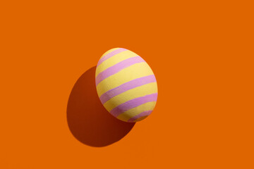 Easter symbol. Festive gift card. Holiday decoration. Abstract background. Colorful egg of yellow and pink striped pattern isolated on orange copy space.