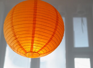 Orange lampshade on glossy ceiling with window reflection.