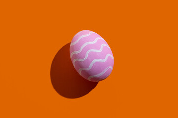 Easter symbol. Festive gift card. Holiday decoration. Abstract background. Pink egg with white zigzag ornament pattern isolated on orange copy space.