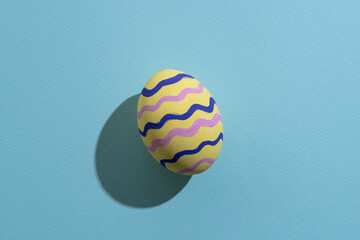 Easter egg. Spring holiday. Gift card. Festive decoration. Yellow painted paschal symbol with colorful zigzag lines pattern isolated on blue textured copy space.