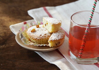 Small homemade cakes with powdered sugar, baked in paper tins with a glass of juice.